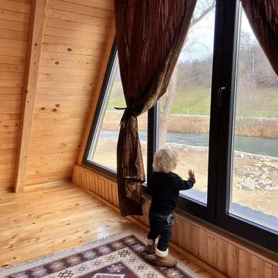 a little boy standing in a room looking out of a window at Vikendica Mia in Šipovo