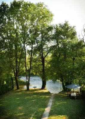 a path next to a lake with trees and an umbrella at Apartmani TIS in Banja Luka