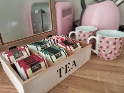a wooden box filled with tea packets next to cups at Cozy Home Apartment Banja Luka in Banja Luka
