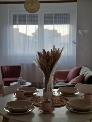 a table with plates and a vase of flowers on it at Cozy Home Apartment Banja Luka in Banja Luka