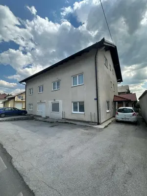 a building with a car parked in a parking lot at Apartman Cypres in Kupres