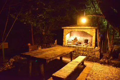 a picnic table in front of a fireplace at night at River house - Riječna idila in Cazin