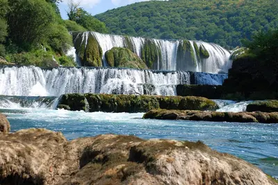 a waterfall in the middle of a river with rocks at New World in Bihać