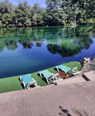 a group of chairs sitting on the grass near a lake at Kuća za odmor Unski Raj in Rudice