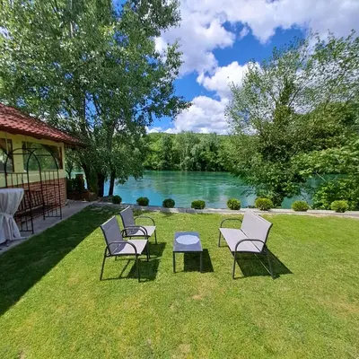 a group of chairs sitting on the grass near a lake at Kuća za odmor Unski Raj in Rudice