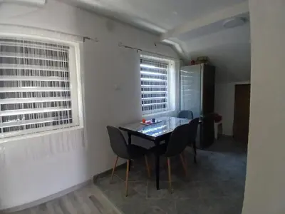 a dining room with a table and chairs and two windows at Stan Nova Varos Banjaluka in Banja Luka